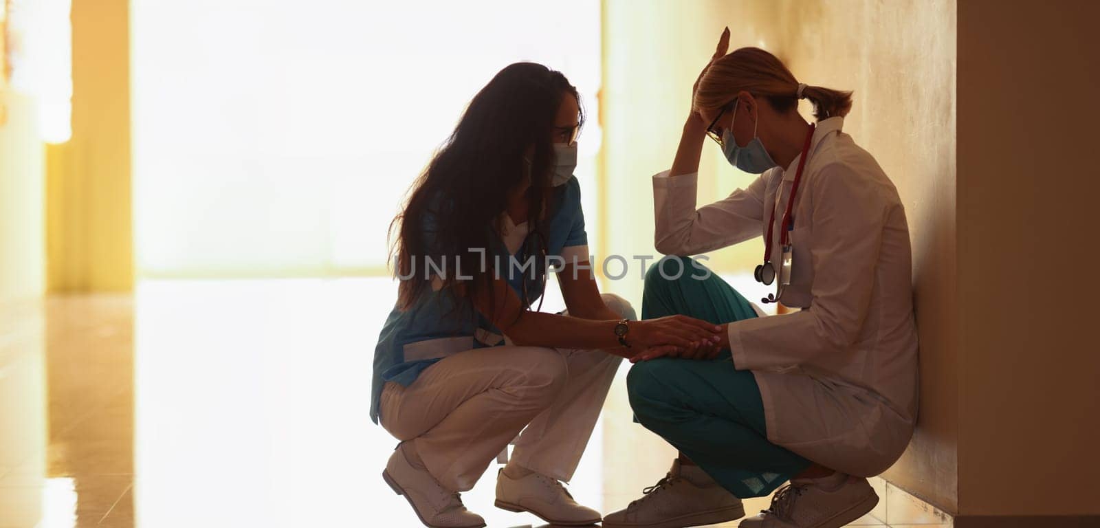A female doctor calms down a tired colleague in the clinic, close-up. Stress of medical staff during a pandemic