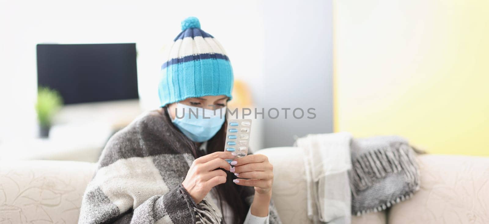 Sick woman in a mask sits in a blanket on the couch, high temperature, close-up. Medicines to treat the virus