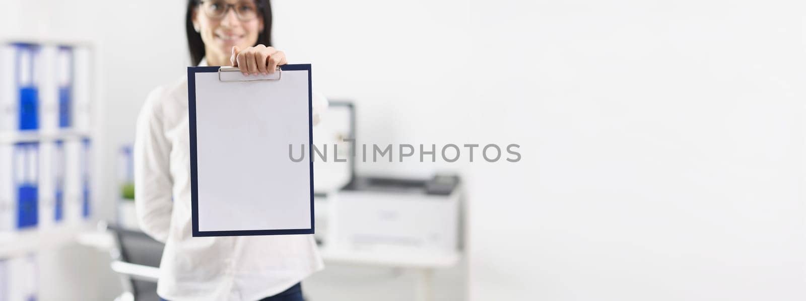 Woman in the office shows a folder with a blank document, mock up, close-up, blurry. Workspace, mentor businesswoman