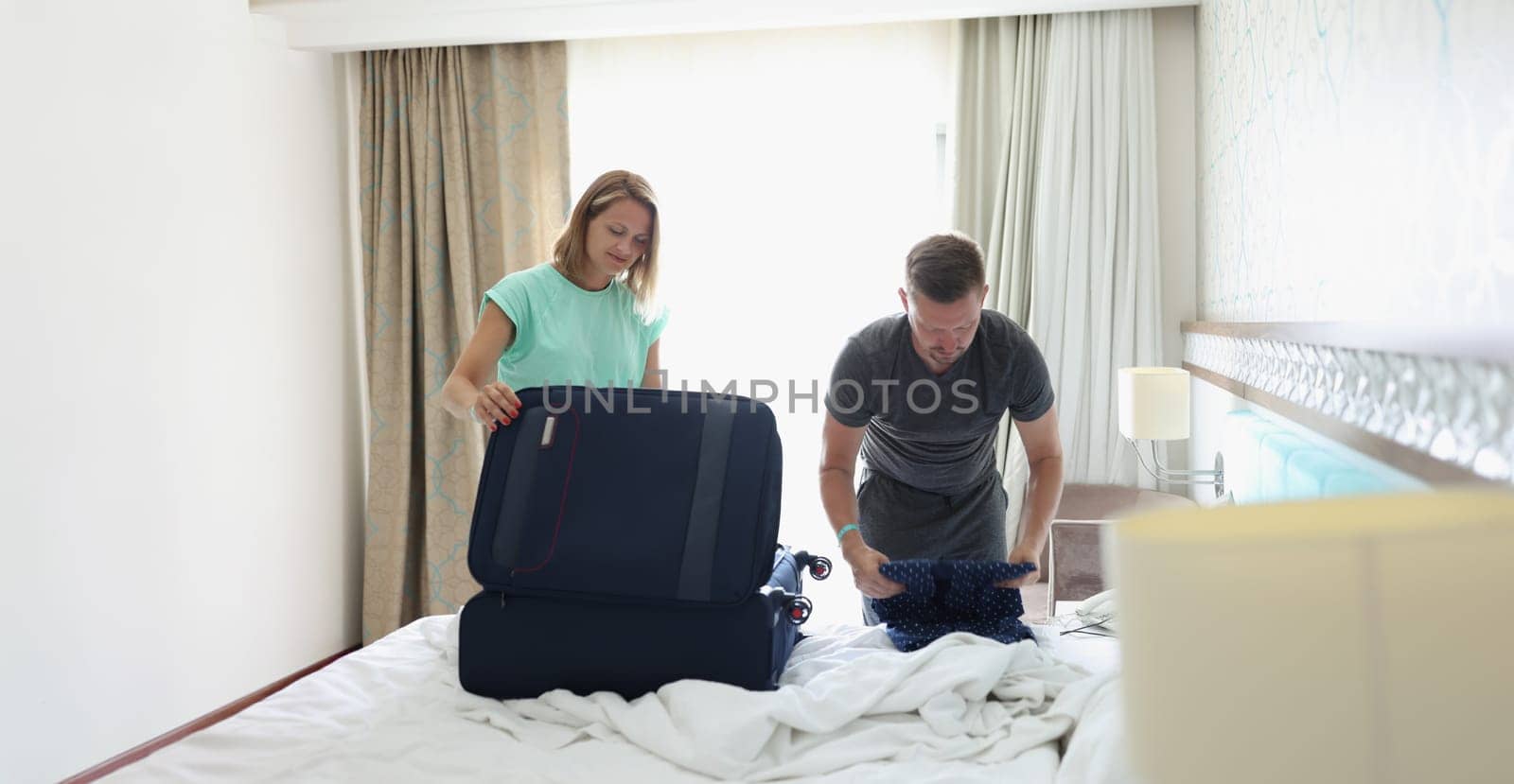 A man and a woman in the room are packing things in a suitcase, close-up. A couple is checked out of the hotel in the morning