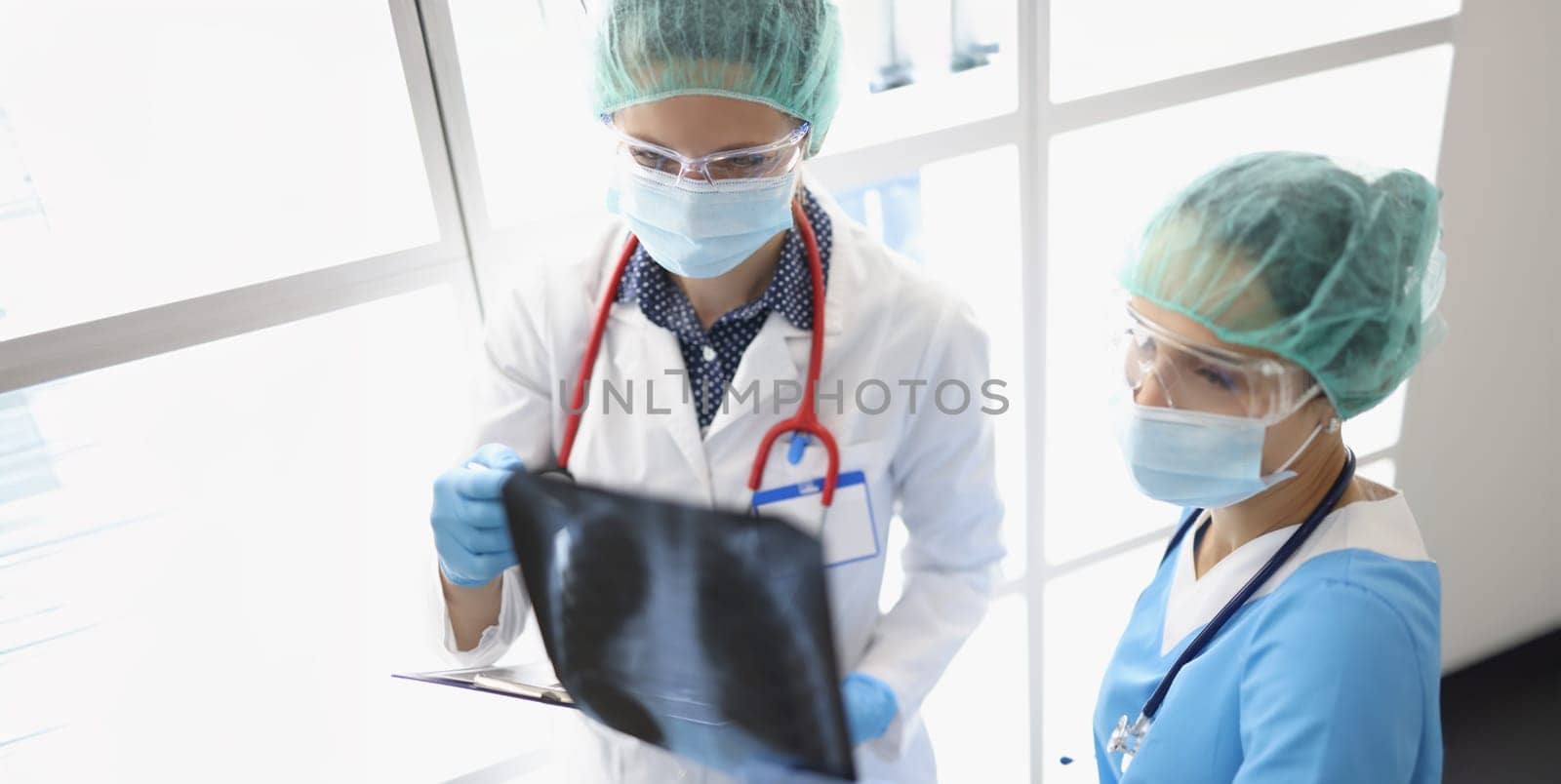 Two female doctors in the clinic are looking at an x-ray of the lungs, close-up. Diagnosis of pneumonia, viral disease, omicron
