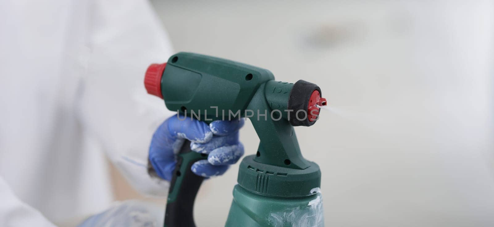 Spray gun in gloved hands, close-up, blurry. Electric construction tool. Wall coating, room renovation