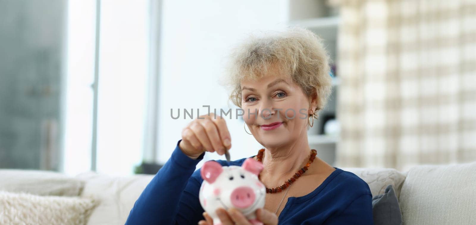 An elderly woman puts a coin in a piggy bank, close-up, blurry. Savings for a retirement fund, saving money