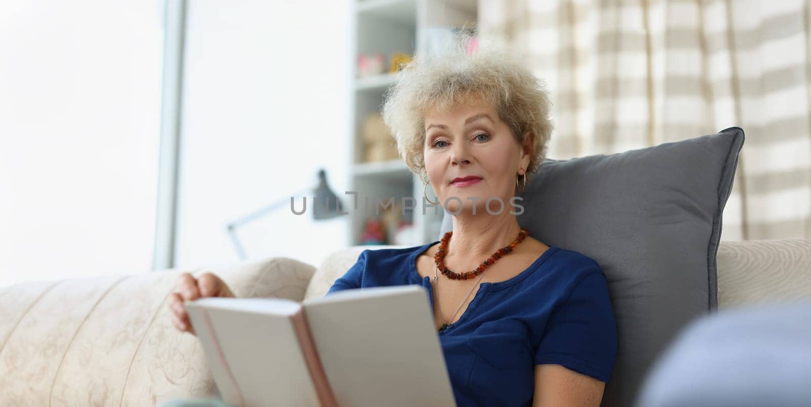 An elderly woman reads a book at home, close-up, blurry. Retirement age, leisure time during a pandemic