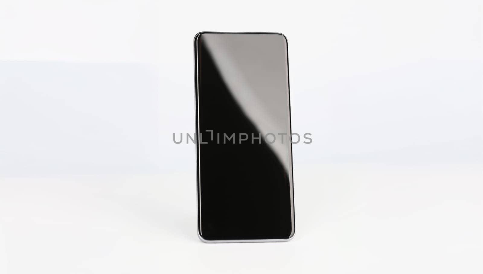 Black smartphone stands upright on a white background, close-up. New device sale, blank screen, digital app, touchscreen