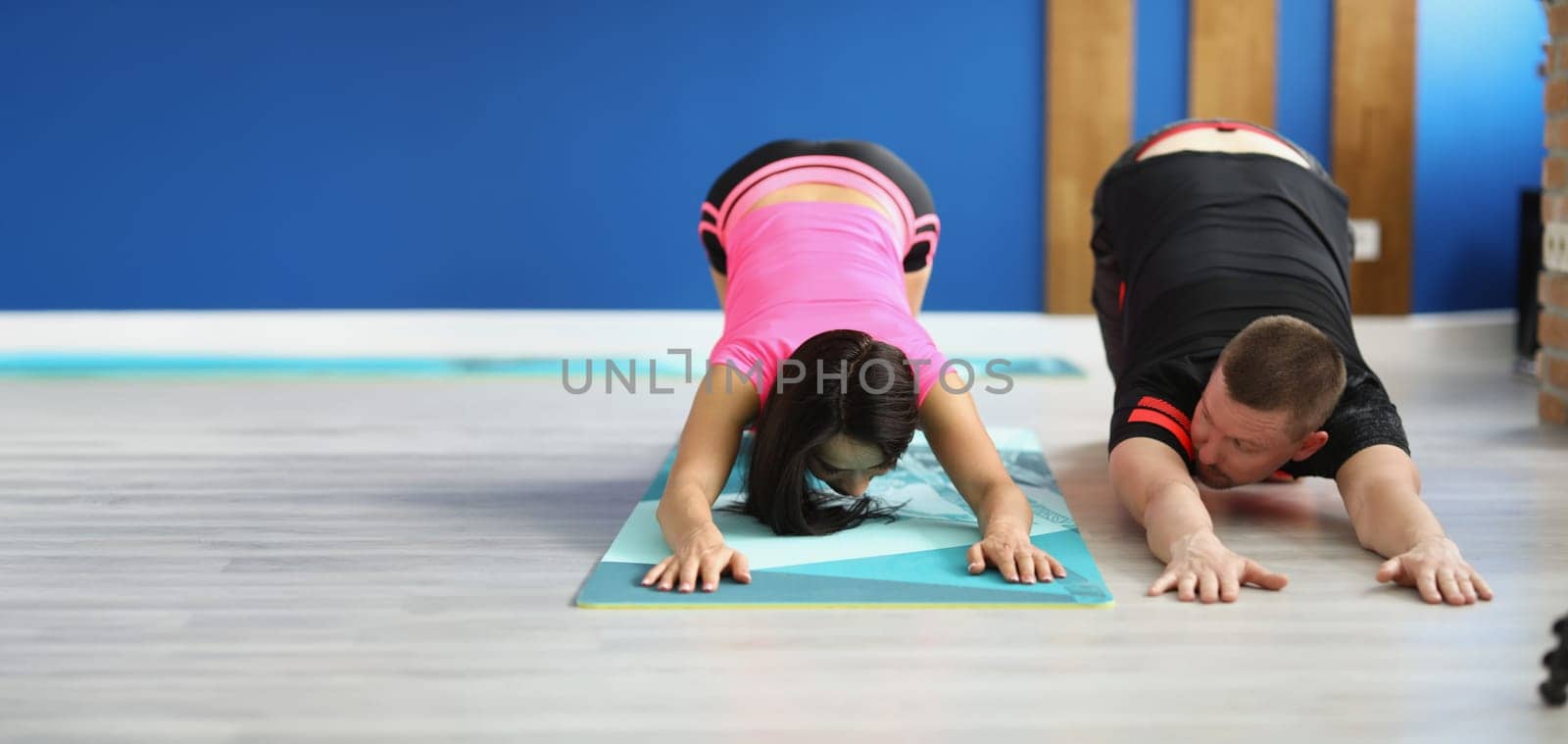 A man and a woman on the floor doing back stretches, close-up. Teaching sports exercises with a trainer in the gym