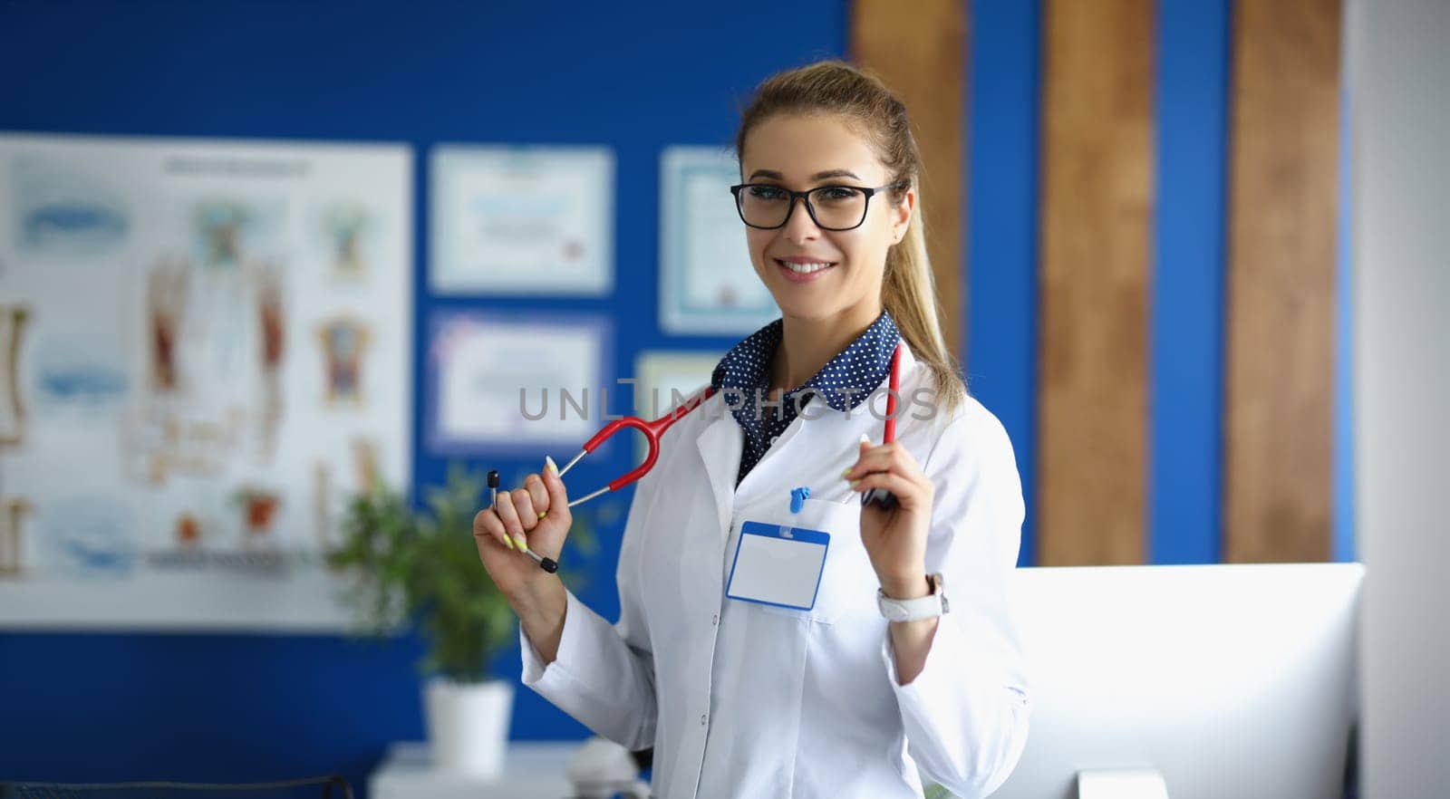 Young woman doctor smiling, standing in the clinic, close-up, blurry. Medical consultation, friendly hospital staff