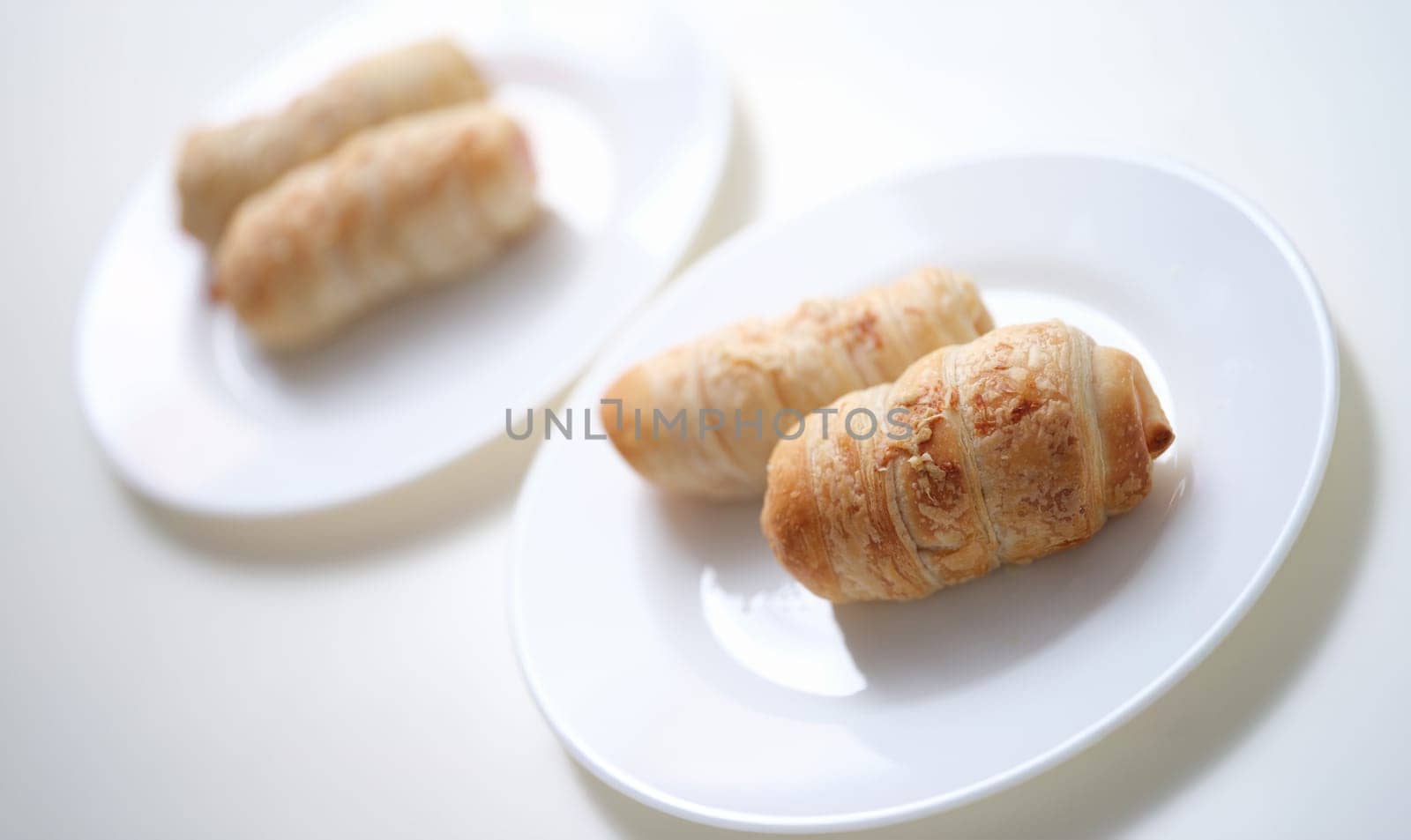 Puff crispy rolls on a white plate, sunny, close-up. Vegan baked goods. Quick breakfast, homemade dessert, pigs blanket