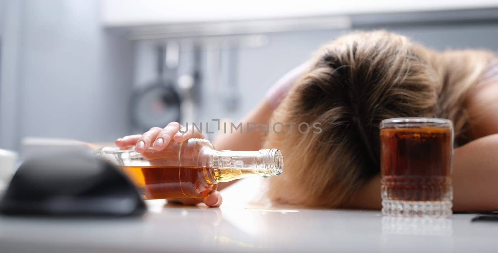 A drunk woman sleeping at the table dropped a bottle of alcohol, close-up. Female alcoholism, a problem in the family