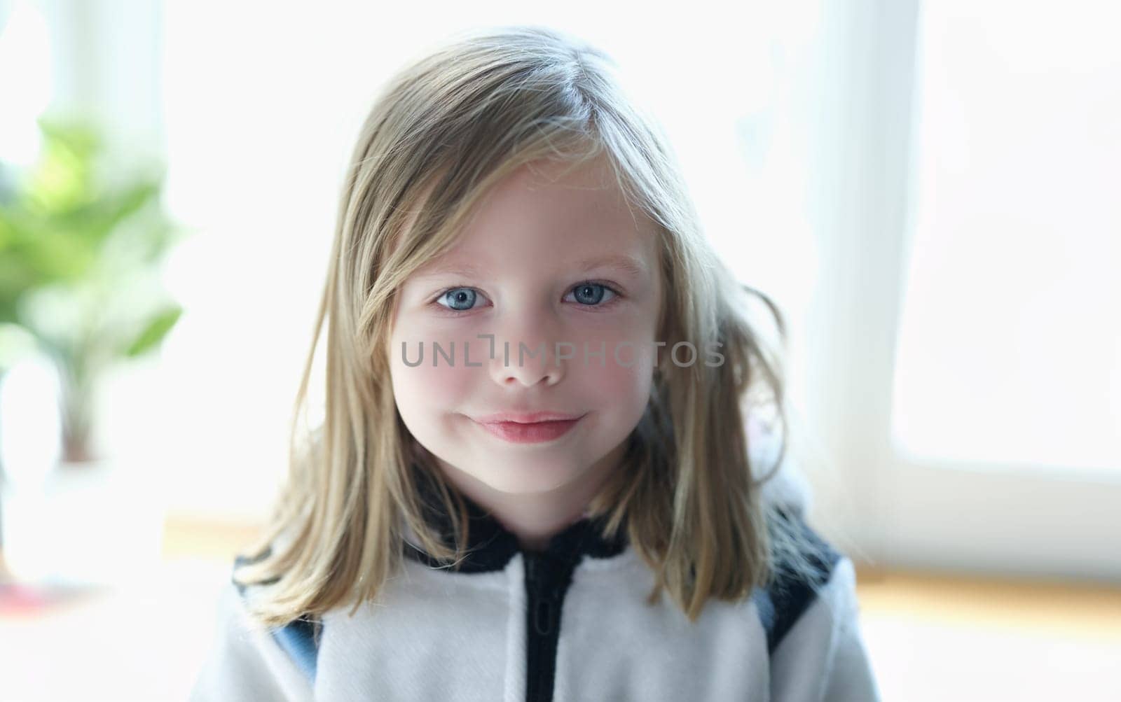 Portrait of a cute blonde girl close-up. Happy child smiles, positive emotions, naive look. The kind face of a little european girl