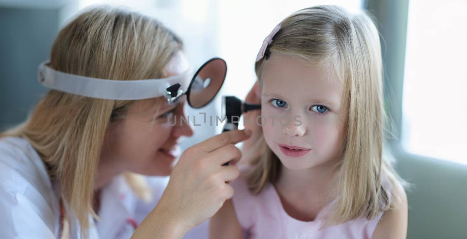 Cute little girl lets the doctor check the woman's ear, close-up, blurry. Pediatrician smiling while examining a child