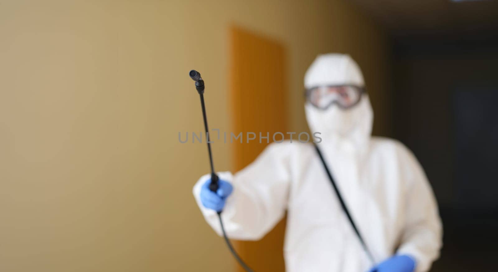 Disinfection specialist in protective uniform with a spray bottle, close-up, blurry. Deratization, deodorization service
