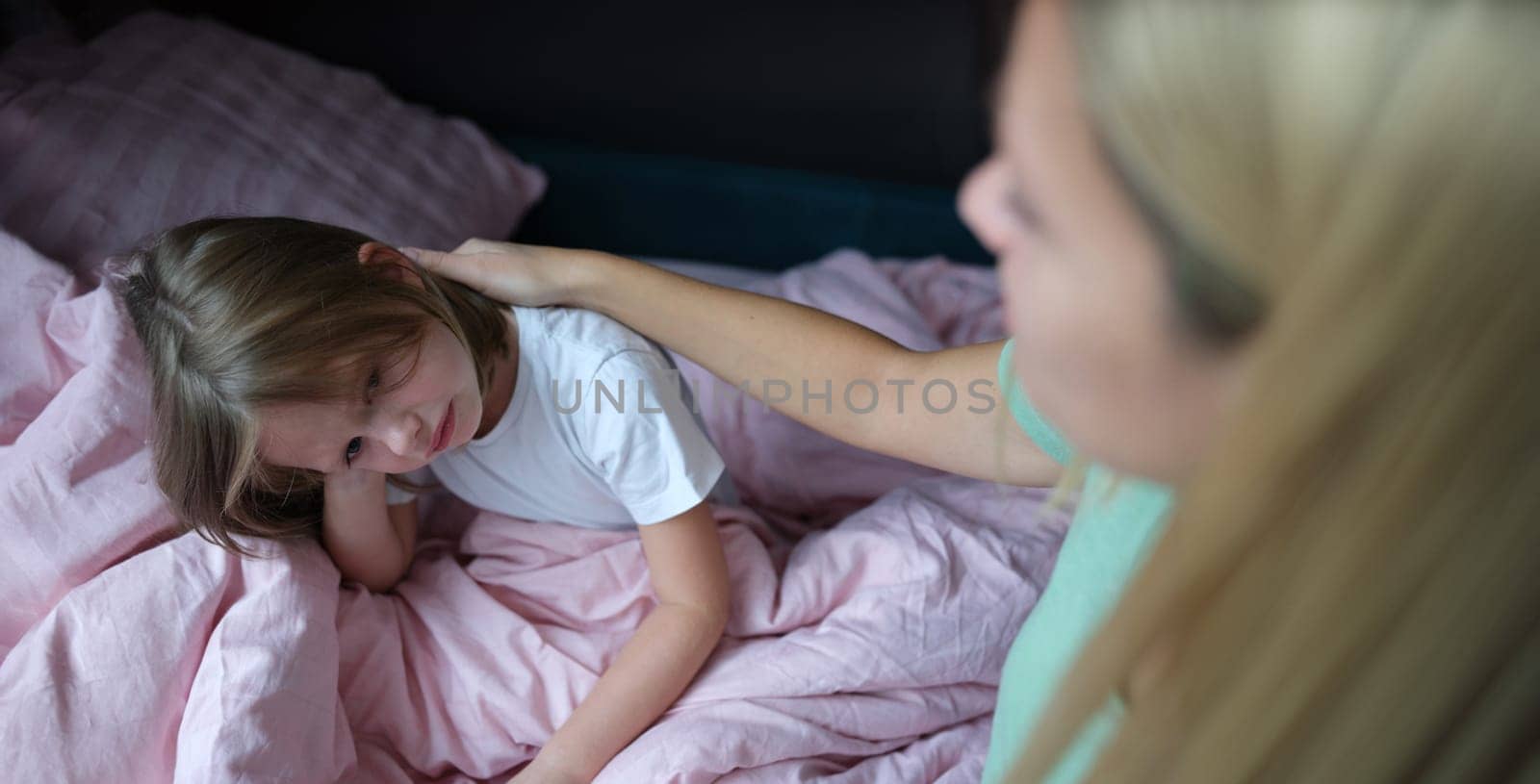 Mom stroking a frustrated little girl on the bed, close-up, blurry. Sad child, insomnia, bad dream, anxiety