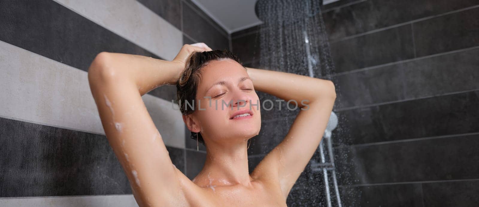 A woman in the shower washes her hair with her eyes closed, close-up. Body cleanliness, daily hygiene, stress relief