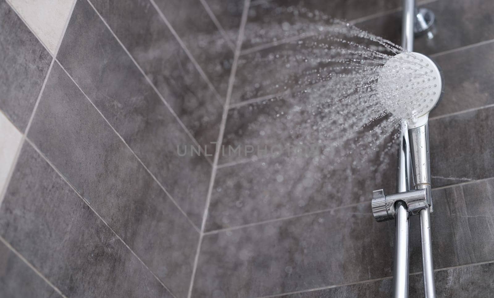 Water is pouring from the shower head into the shower room, close-up. Refreshing shower, cleanliness and hygiene