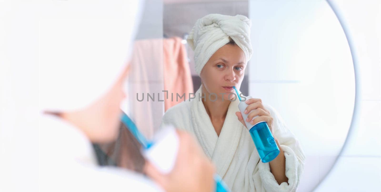 A woman in a dressing gown with a towel on her head is brushing her teeth with an irrigator. Oral hygiene, beauty and health