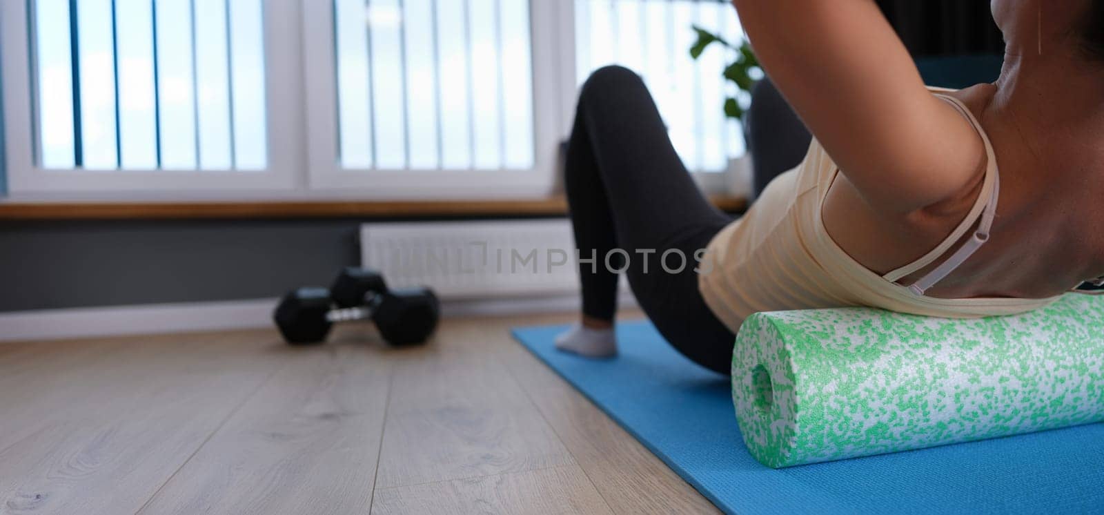 A woman lies on a sports roller, does exercises for the back at home, close-up. Fitness during quarantine