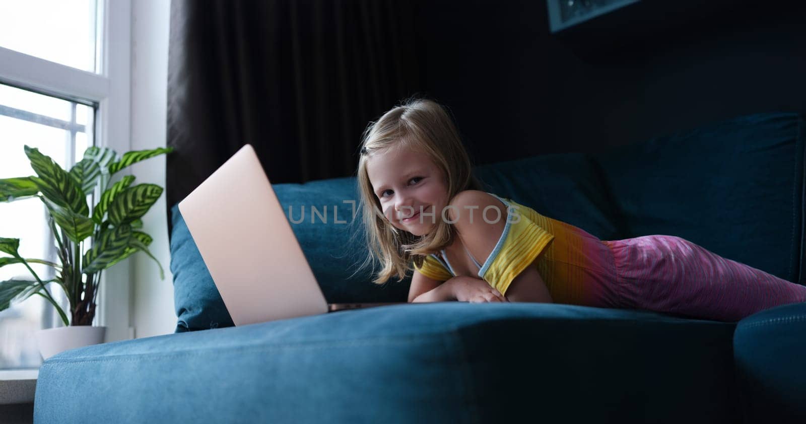 Happy little girl lies on the couch in front of a laptop, close-up. Child uses the Internet, cybersecurity