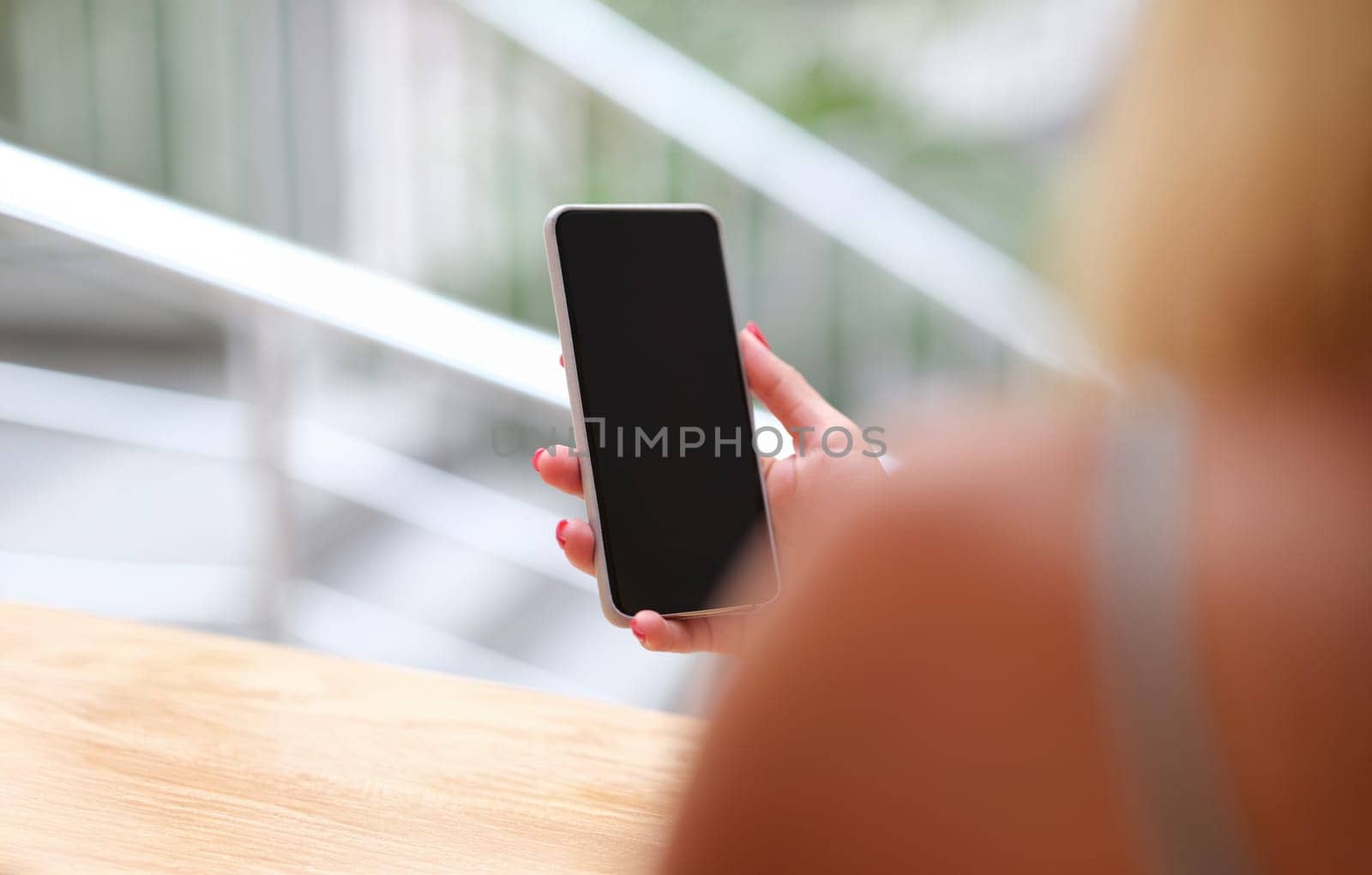 Woman holding a smartphone, sunny, hands close-up. The view from the back is blurry. Mobile phone black screen, mock up