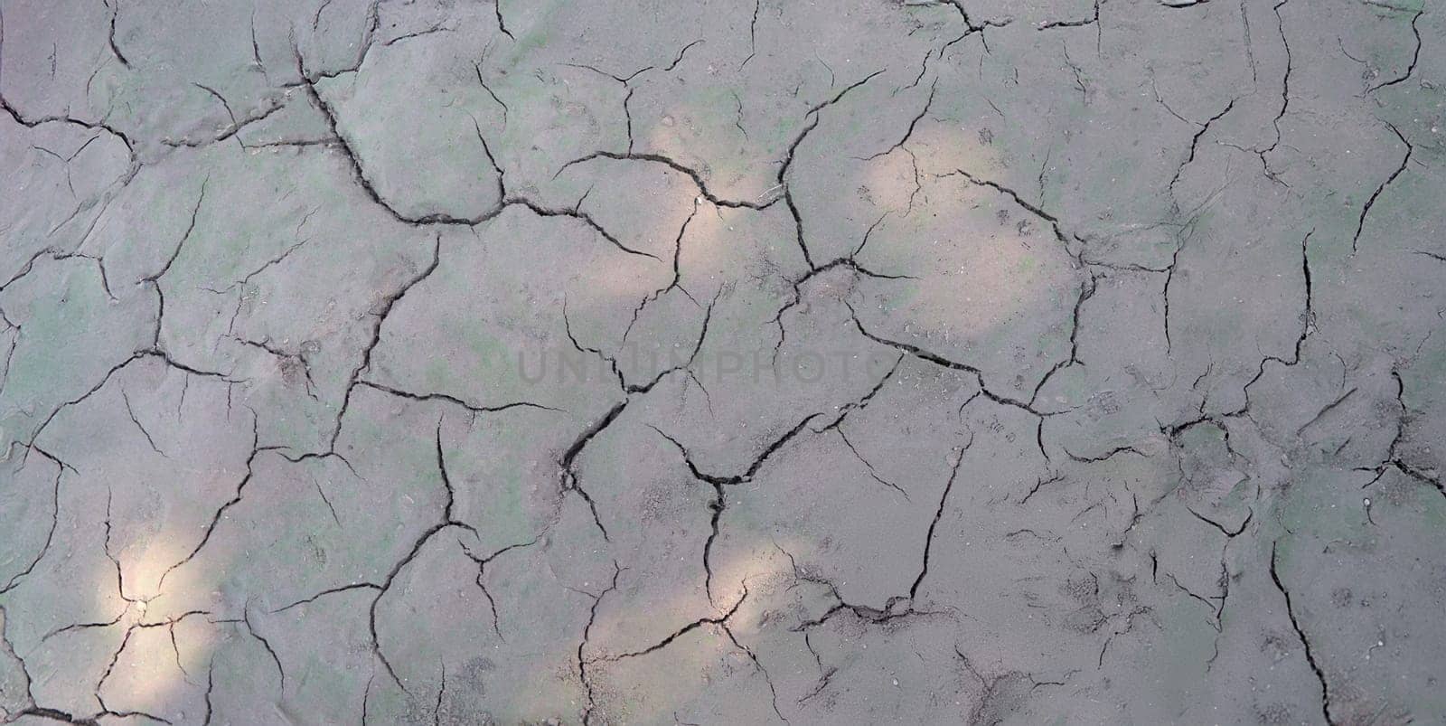Sun beams on dry cracked gray ground, close-up. Soil erosion, drought, poor ecology, lack of rainfall