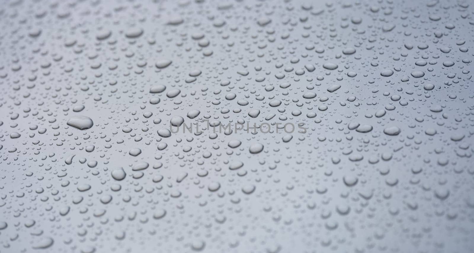 Small droplets of water on a matte gray background, close-up. Rain on a flat surface, condensation on glass