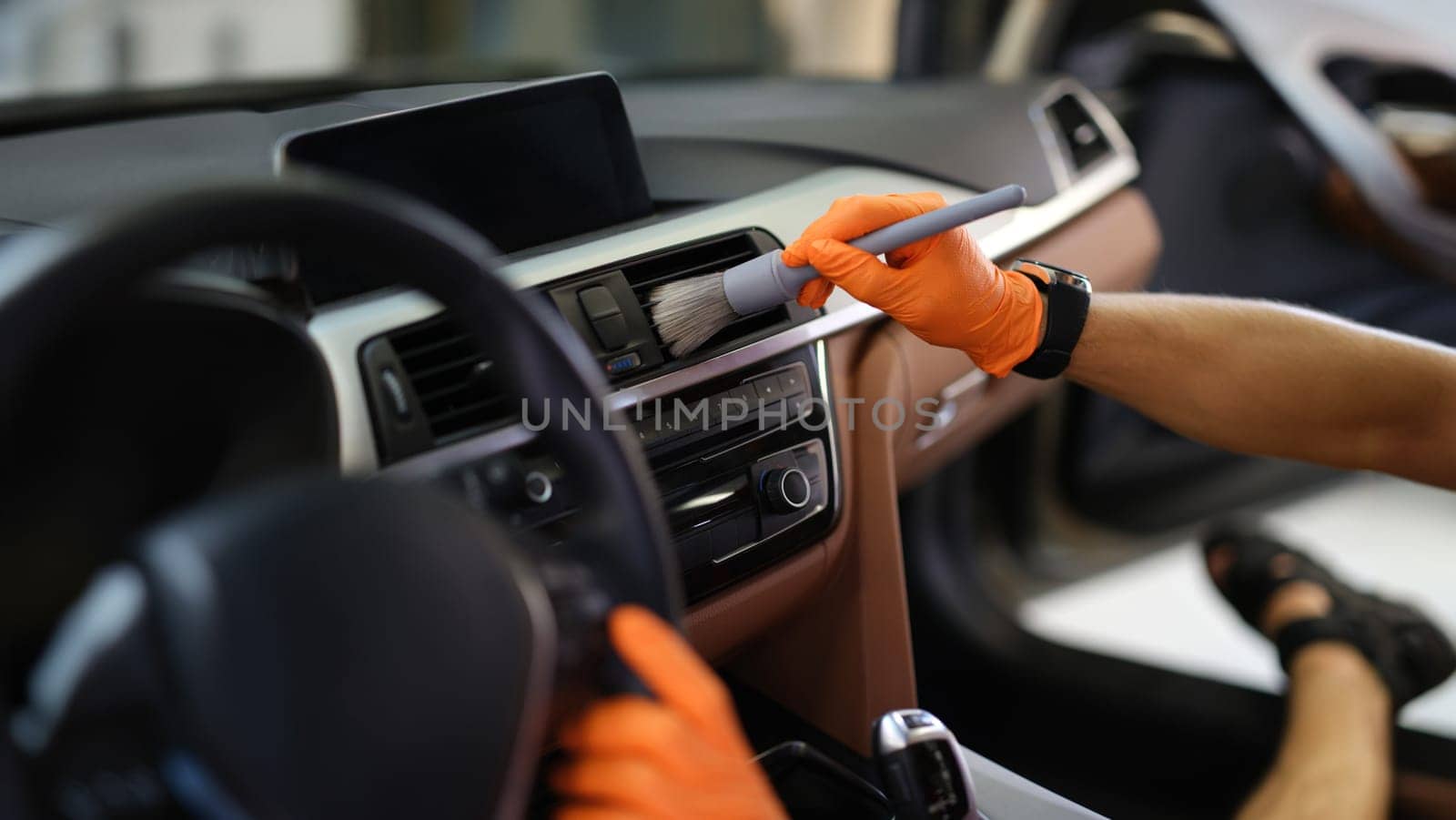 Male hands brush dust from the ventilation system in the car, close-up. Car interior, professional car cleaning service