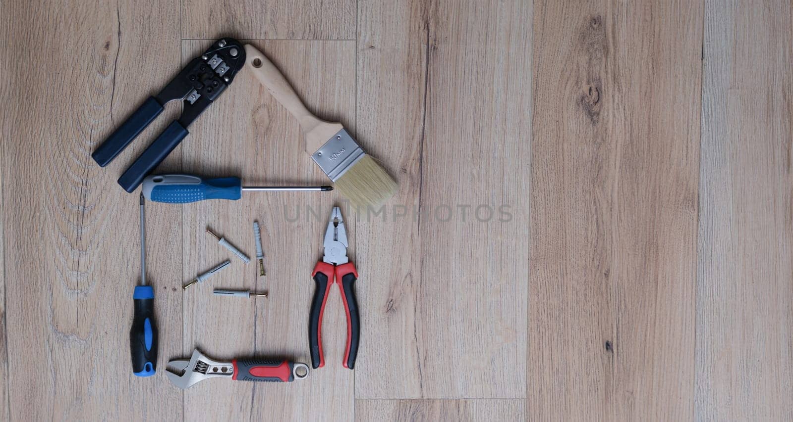 A set of tools for home renovation lies on the laminate. Adjustable wrench with screwdriver. Pasatizhi and paint brush.