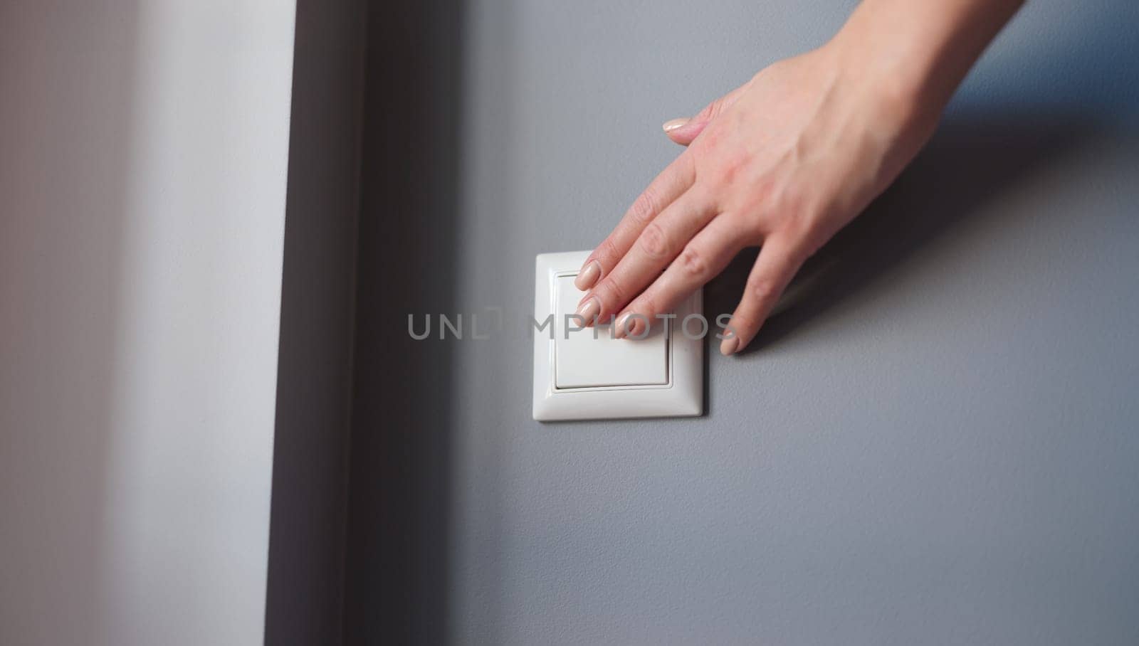 A woman's hand presses the switch on the wall, close-up. White light switch on gray wall background, checking electricity