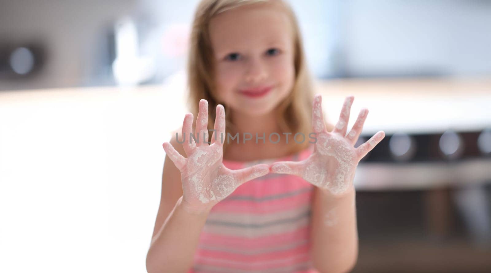 Little cute girl shows palms in flour, close-up, blurry. Teaching kids how to cook, online course on cooking at home