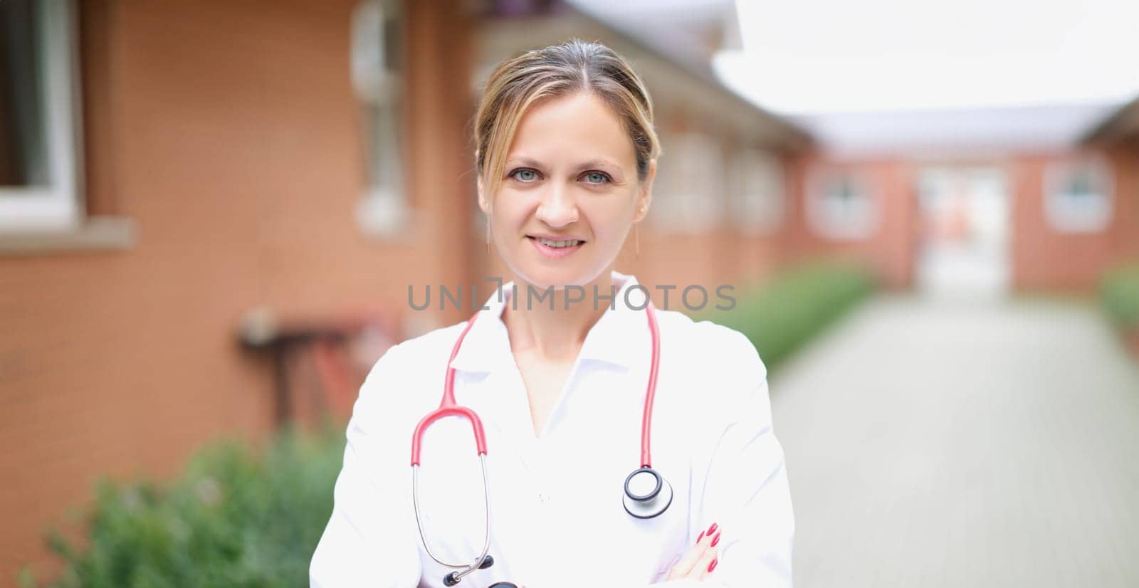 Doctor, a beautiful woman stands on the street against the background of the hospital, close-up, blurry. Ambulance service, clinic staff