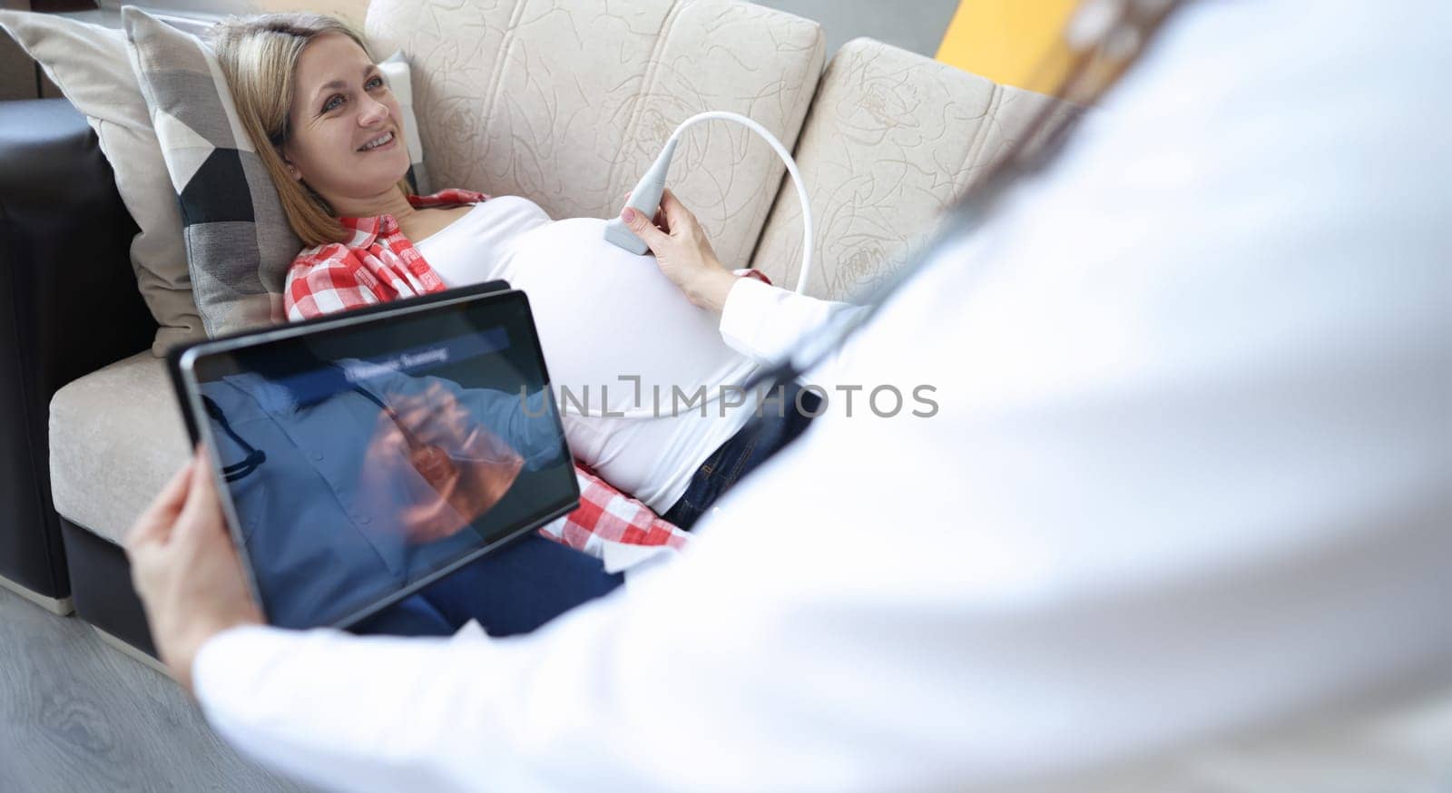 Doctor doing ultrasound of fetus to pregnant woman at home. Modern technologies in medicine concept