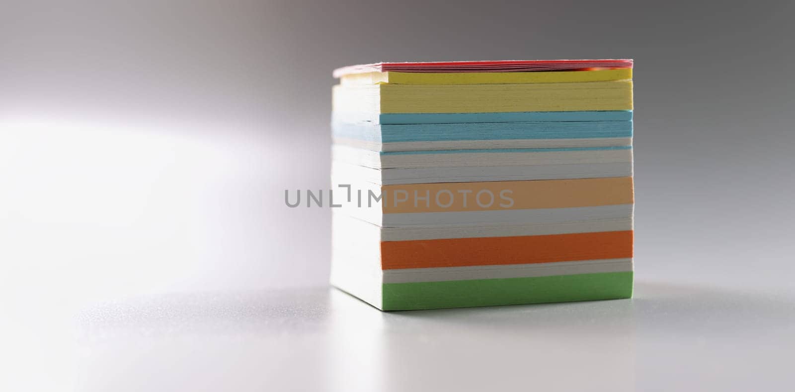 Multi-colored stack of paper for notes on a gray background, close-up. Different color blank post notes