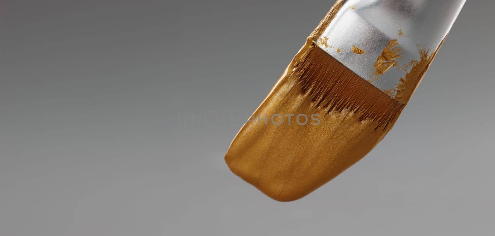 Brush with gold paint on a gray background, close-up. Shiny golden texture of paint on the bristles of a painting brush