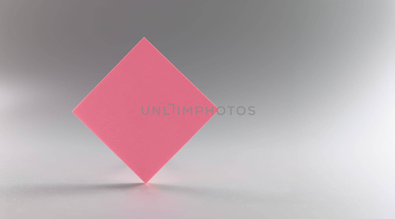 Pink blank paper rhombus on a gray background, close-up. beautiful design element, sheet sticker, branding