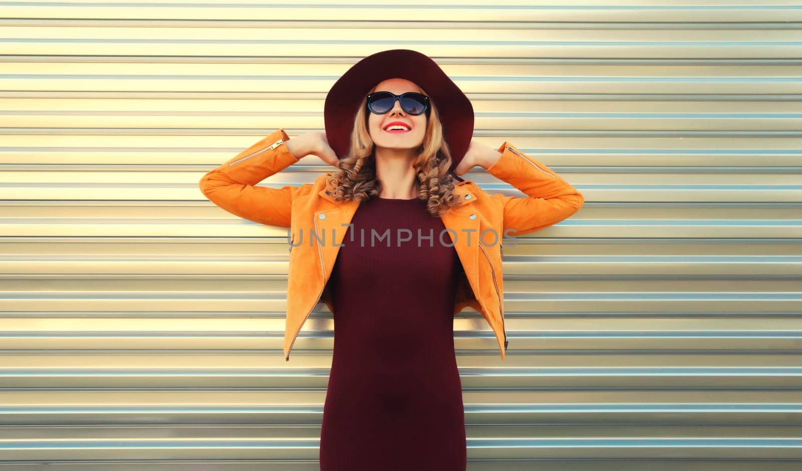 Beautiful happy smiling young woman wearing orange jacket, round hat on gray background
