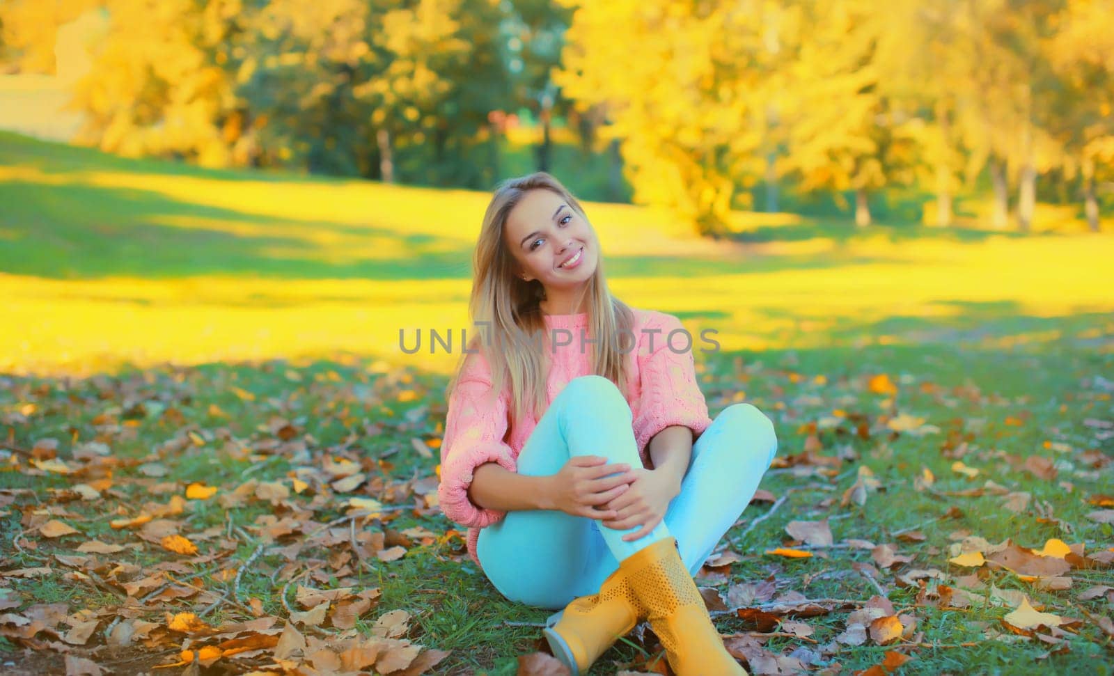 Beautiful young woman wearing pink sweater sitting in autumn park
