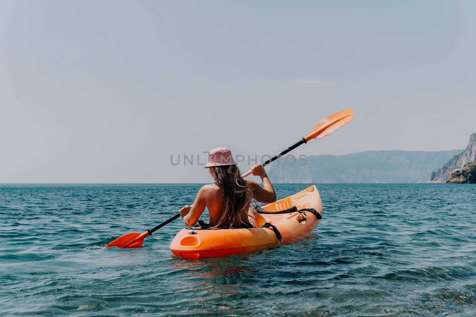 Happy smiling woman in kayak on ocean, paddling with wooden oar. Calm sea water and horizon in background