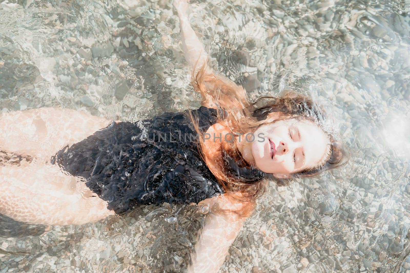 A woman with long hair floats on her back in crystal clear water, enjoying a moment of relaxation.