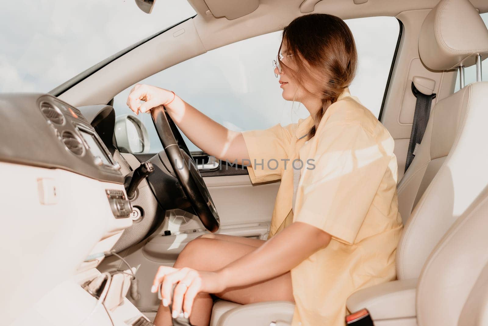 A young woman with brown hair, wearing sunglasses and a yellow shirt, sits behind the wheel of a car, her expression focused on the road ahead.