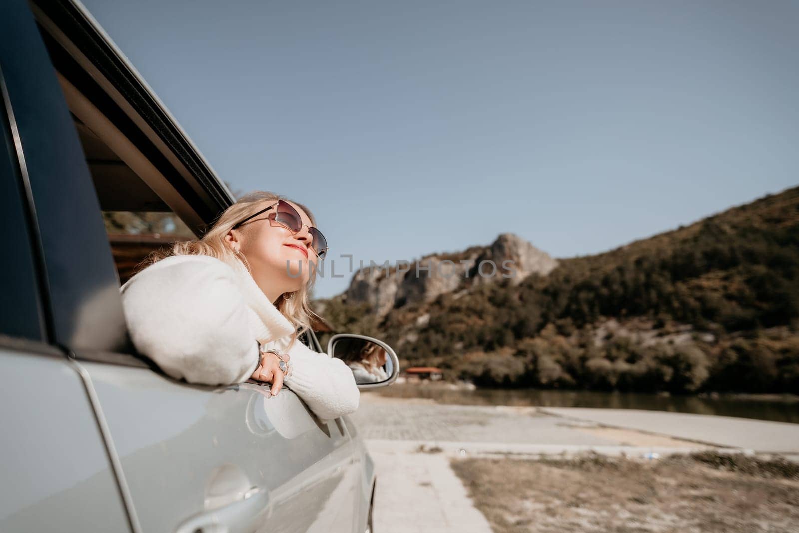 A woman with sunglasses looks out the car window while driving through a scenic mountain area.