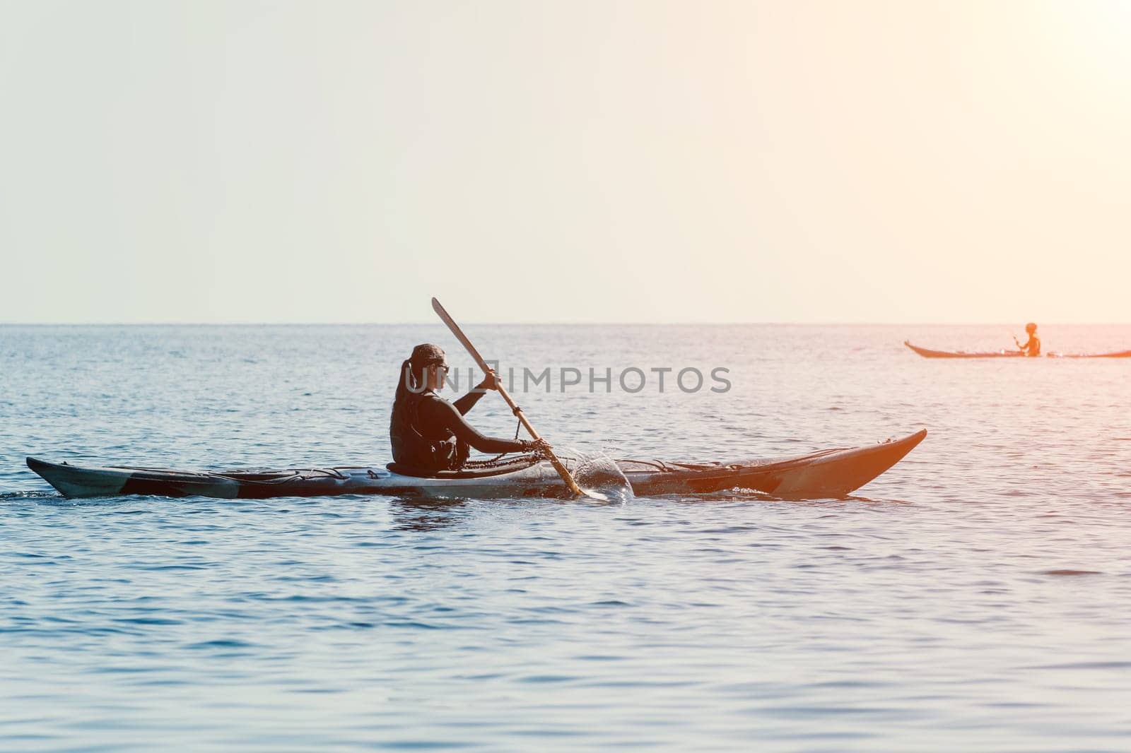 Happy smiling woman in kayak on ocean, paddling with wooden oar. Calm sea water and horizon in background