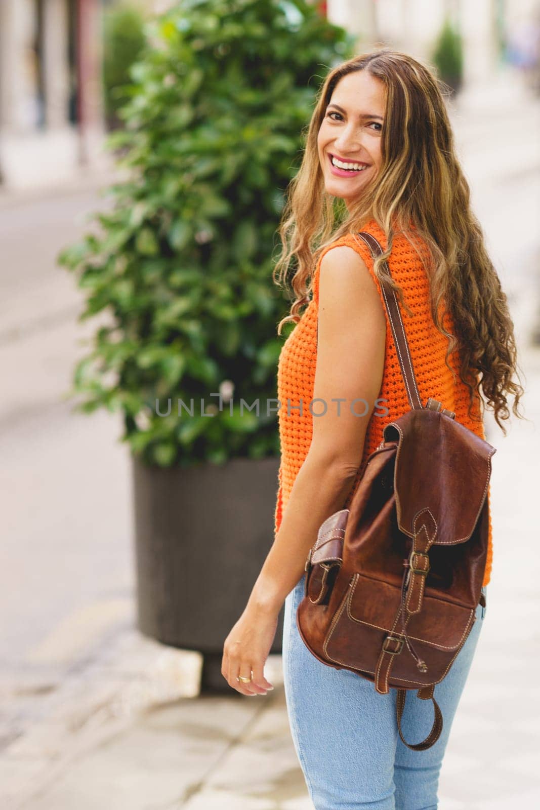 Vertical photo of a charming latin woman turning to smile while walking down the city