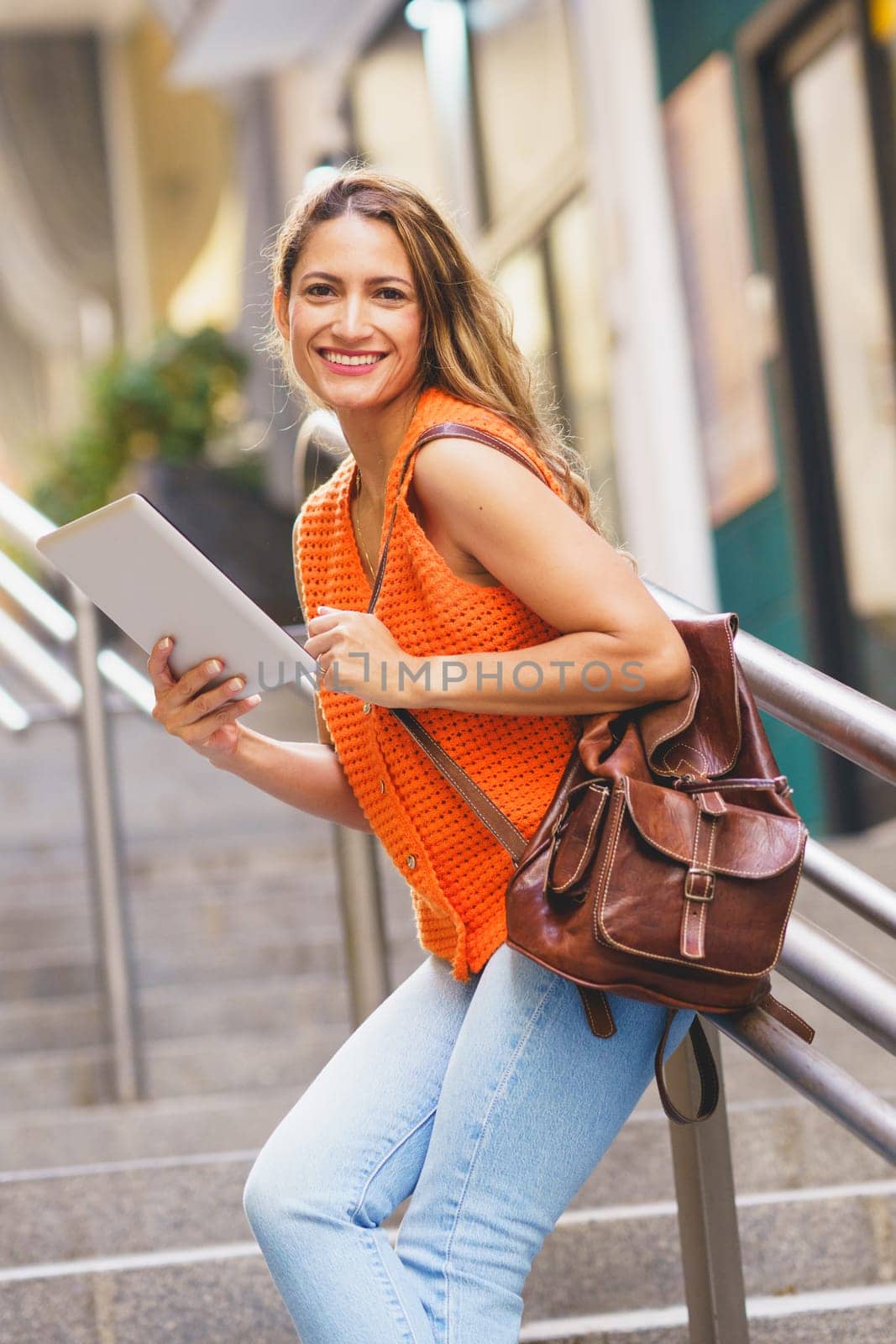 Vertical low angle view photo of a happy female latin student using tablet leaning on outdoors urban stairs