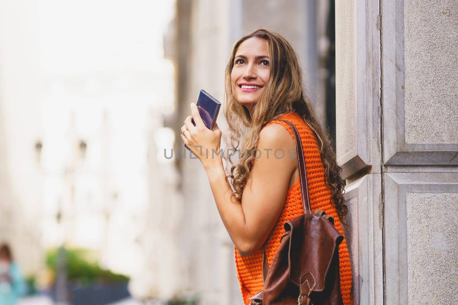Latin beauty woman holding a mobile phone and looking up visiting a city
