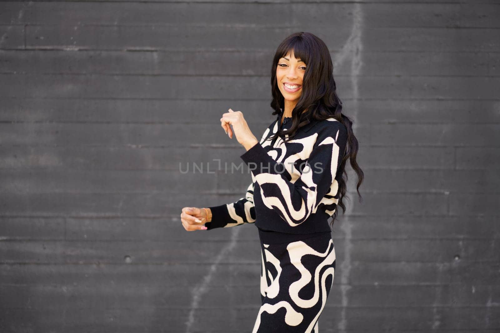 Happy confident female hispanic artist in black and white modern clothes dancing in the city
