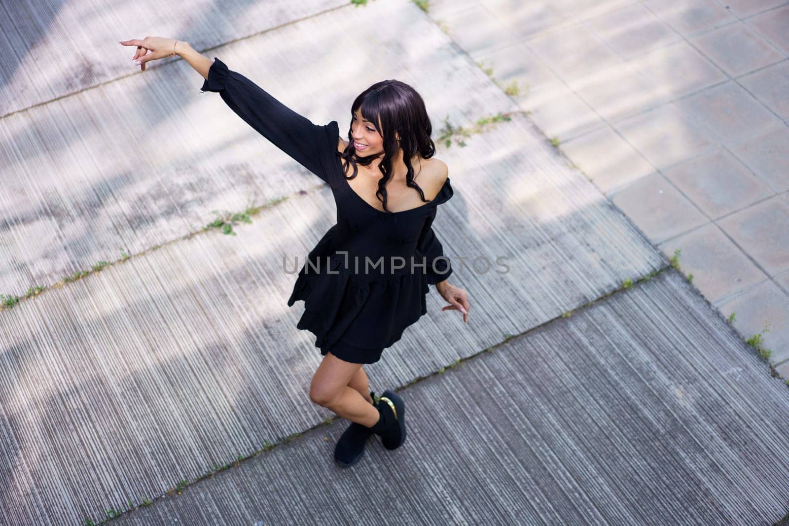 View from above of an energetic woman dancing a choreography wearing black summer dress outdoors in the street