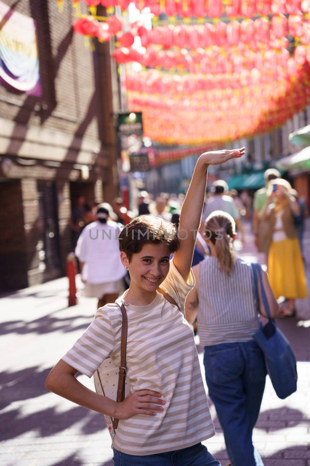 A vibrant and lively scene in Chinatown showcases a young person posing joyfully amid the bustling crowds and beautifully colorful lanterns that decorate the area, creating a festive atmosphere