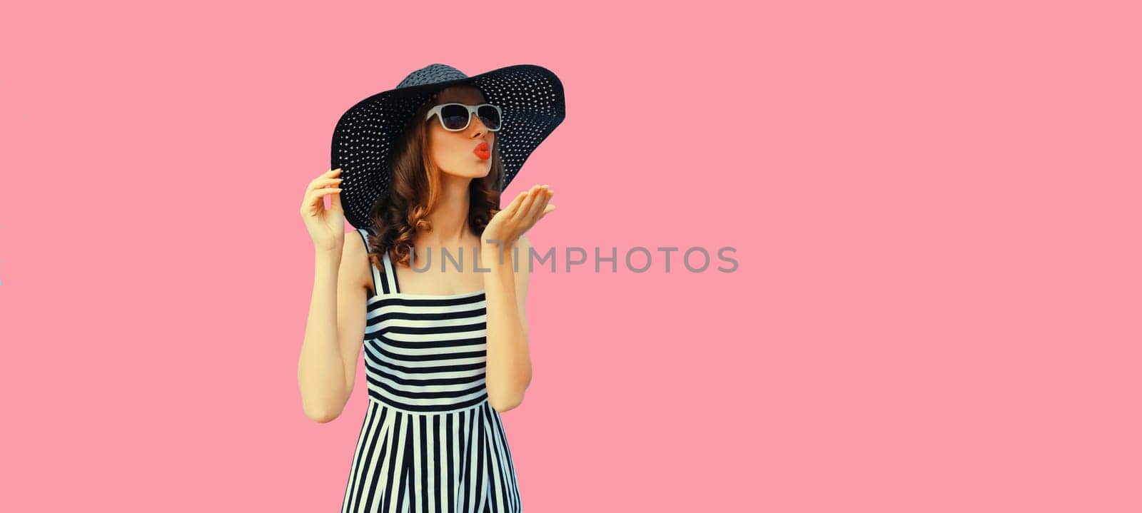 Summer portrait beautiful young woman model blowing kiss in black round straw hat on pink background