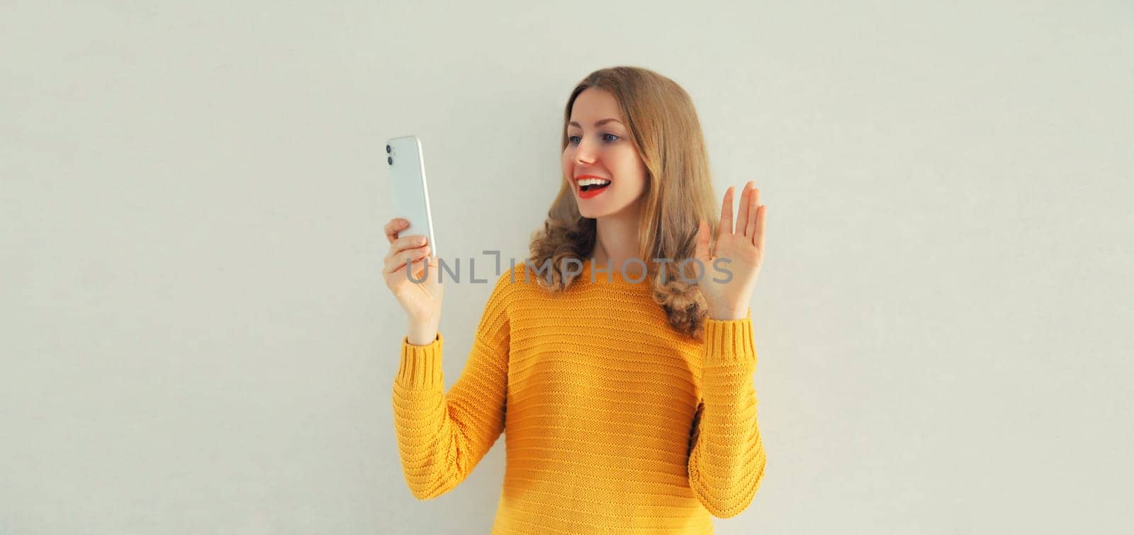 Happy smiling young woman taking selfie with phone or talking on video call waving hand on white