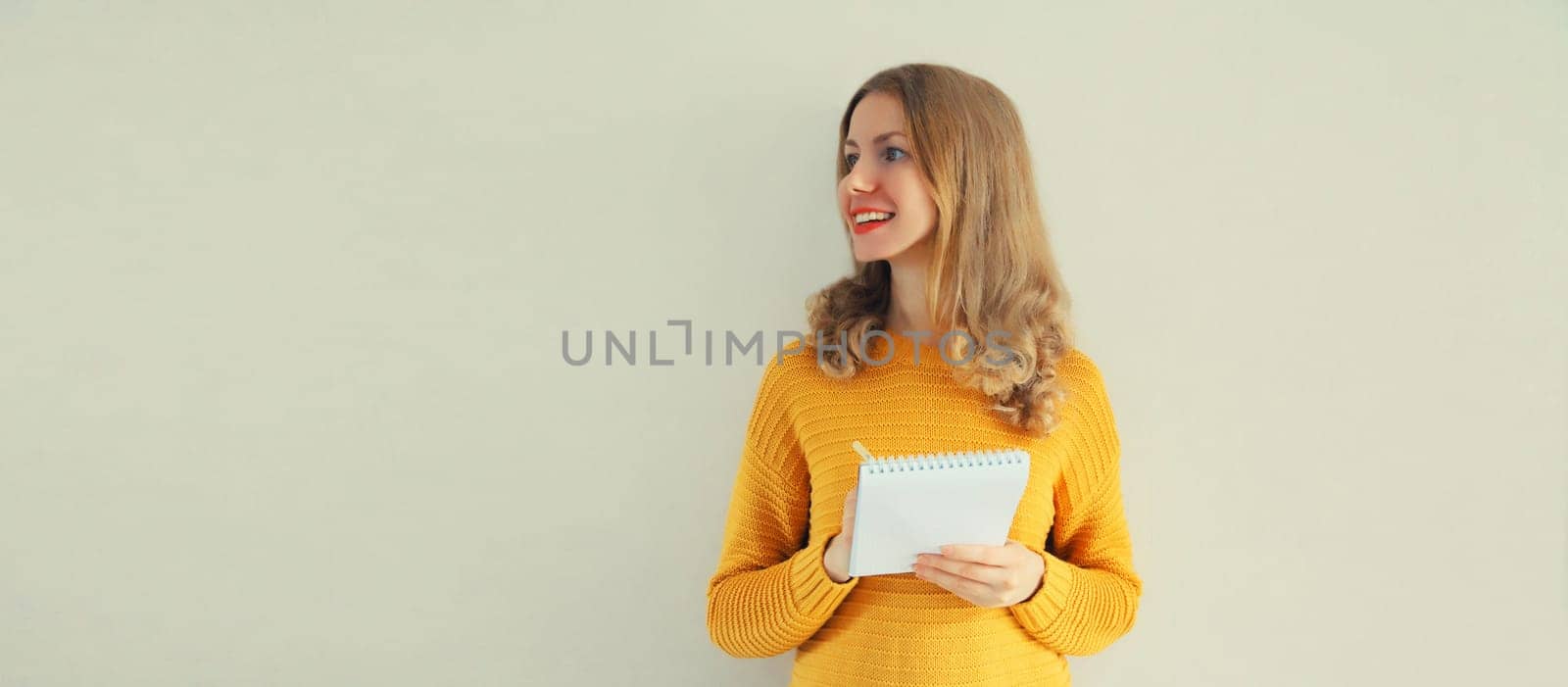 Portrait of young caucasian woman writing down memories in notebook diary on gray background